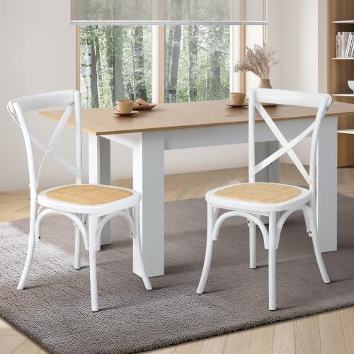 Two white crossback dining chairs with solid rubberwood frame and rattan seats, placed around a wooden table in a room with a window.